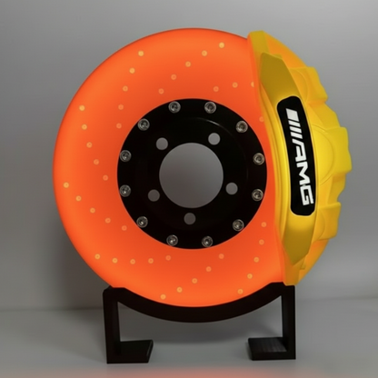 Orange brake disc with yellow hub and AMG logo on a black stand against a dark background